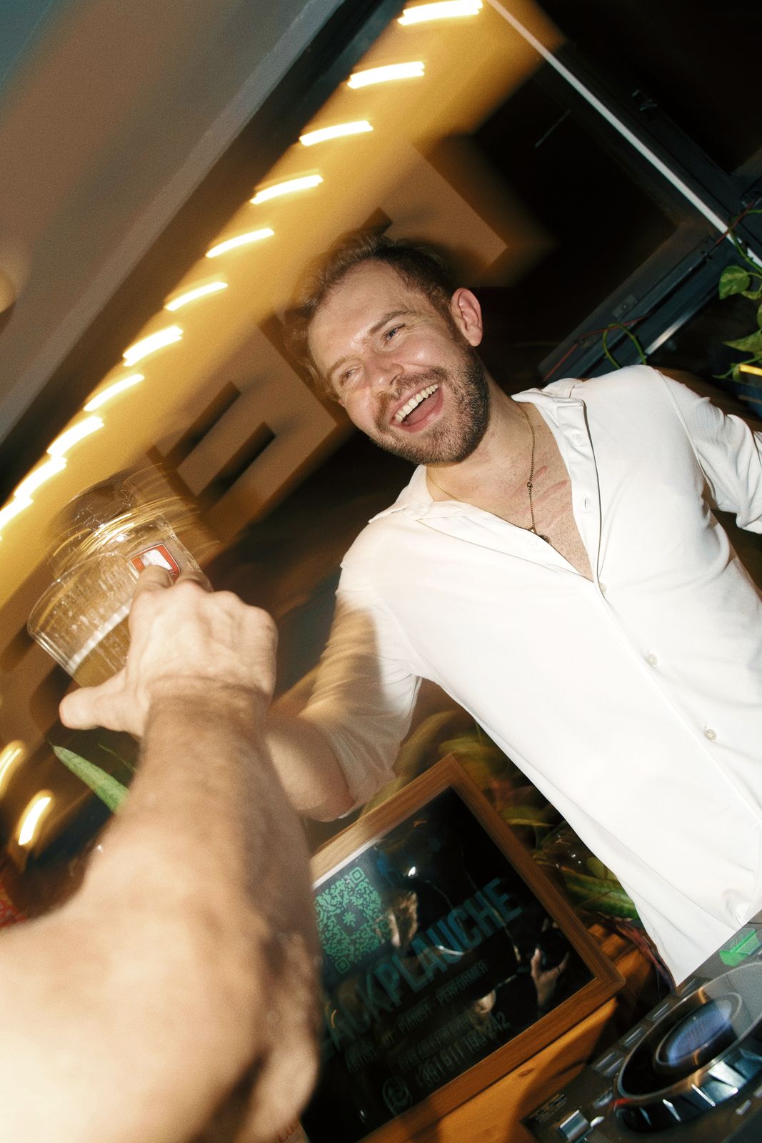 Zack laughing and raising a beer at a DJ gig